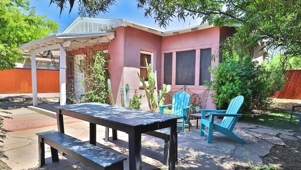 Un patio con mesa y sillas, un espacio de estar techado y una planta de cactus.