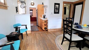 Una cocina compacta con armarios de madera, una zona de comedor con una mesa redonda y sillas, y un acceso visible a otra habitación.