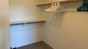 A small, enclosed closet with two wooden rods, one with white hangers and one with blue hangers. - Thunder Ridge (Tucson)