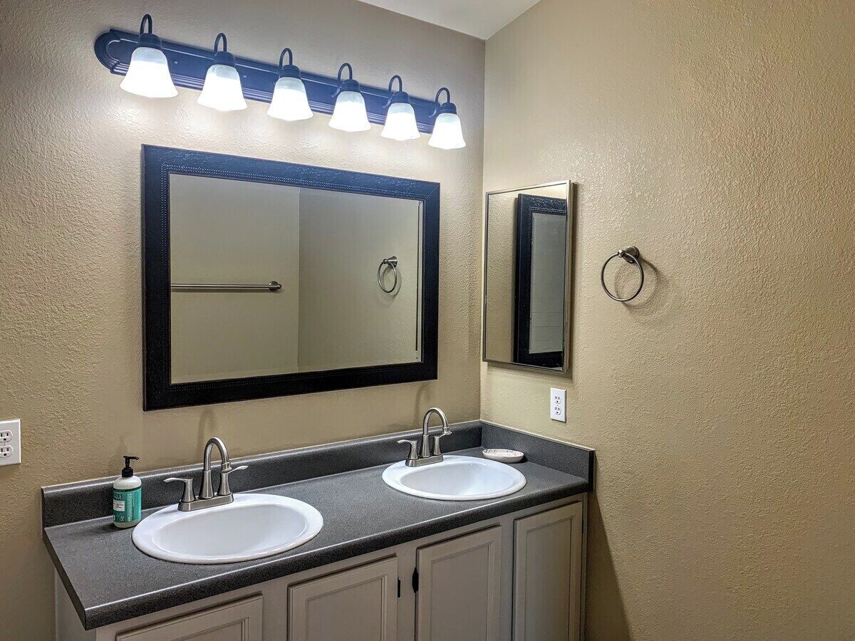 A bathroom with two sinks, a large mirror, and a light fixture above the mirror.