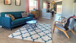 A living room with a blue sofa, a coffee table, and a patterned rug. There is a dining area in the background with a table and chairs. - Thunder Ridge (Tucson)
