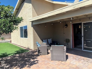 An outdoor patio with wicker furniture, a glass door entrance, and a small window. - Thunder Ridge (Tucson)