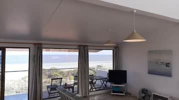 Een ruime woonkamer met een grote schuifpui naar een balkon, een flatscreen televisie, een plafondventilator en een schilderij aan de muur.