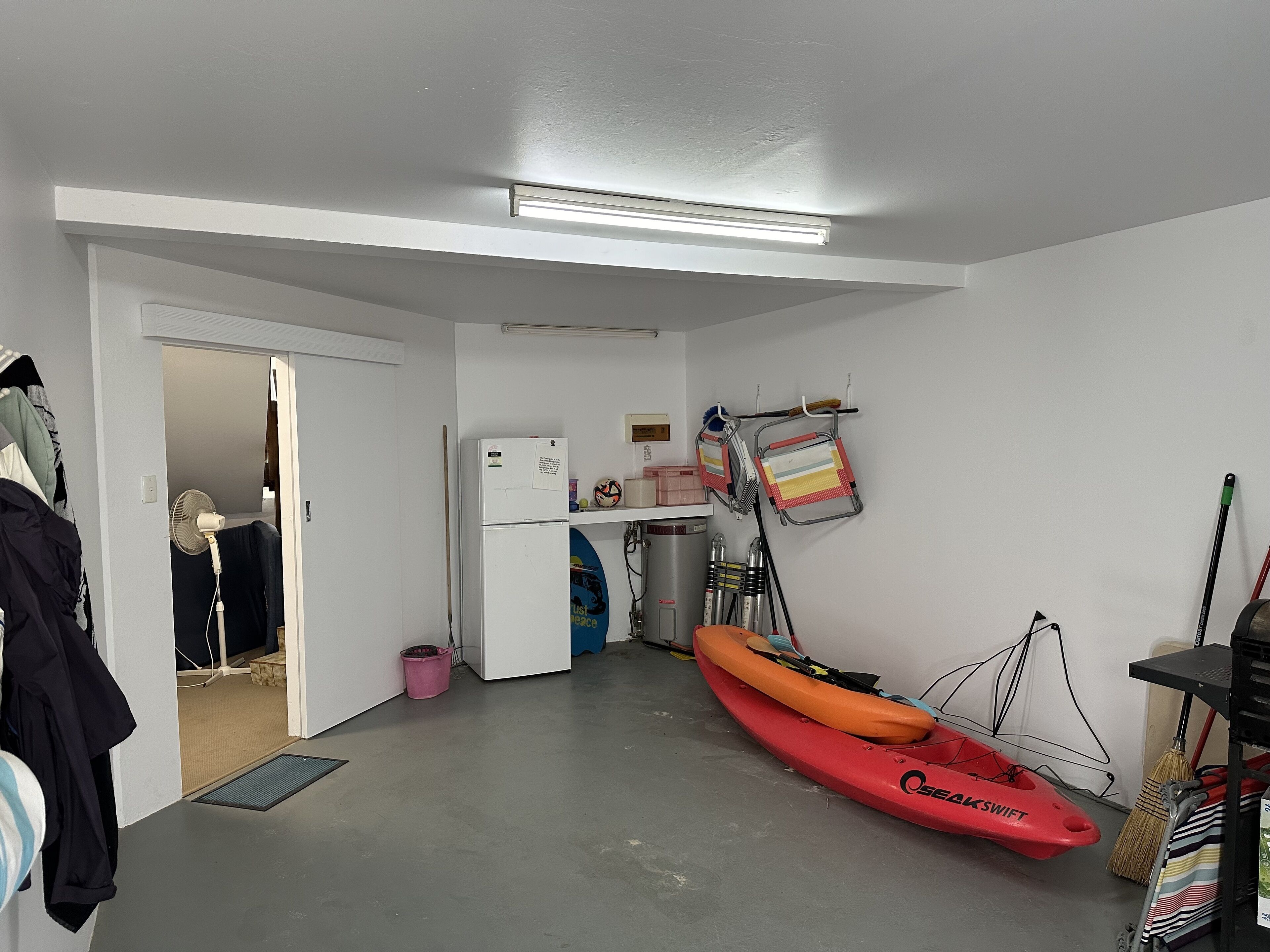 A compact kitchen with a refrigerator, a fan, and a kayak.