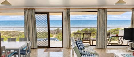 A spacious living area with a large sliding glass door leading to a balcony with a view of the ocean.