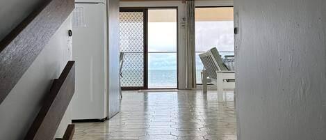 A hallway leading to a balcony with a view of the sea, a refrigerator, and a wooden bench.