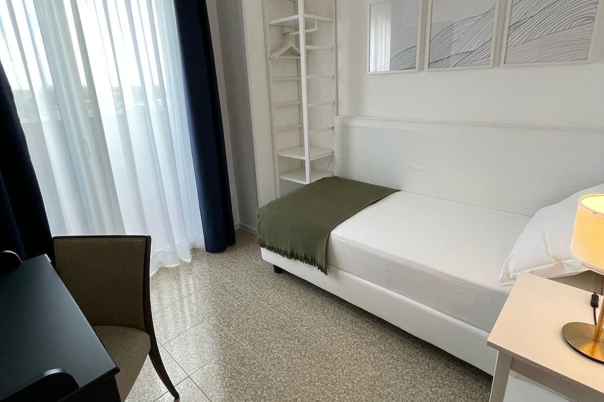 A hotel room with a bed, a desk, a chair, a wardrobe, and a window with curtains.