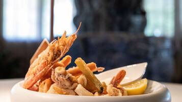 Une assiette de fruits de mer, accompagnée d’une tranche de citron et d’un petit bol de sauce, est posée sur une table, avec une lampe en arrière-plan.