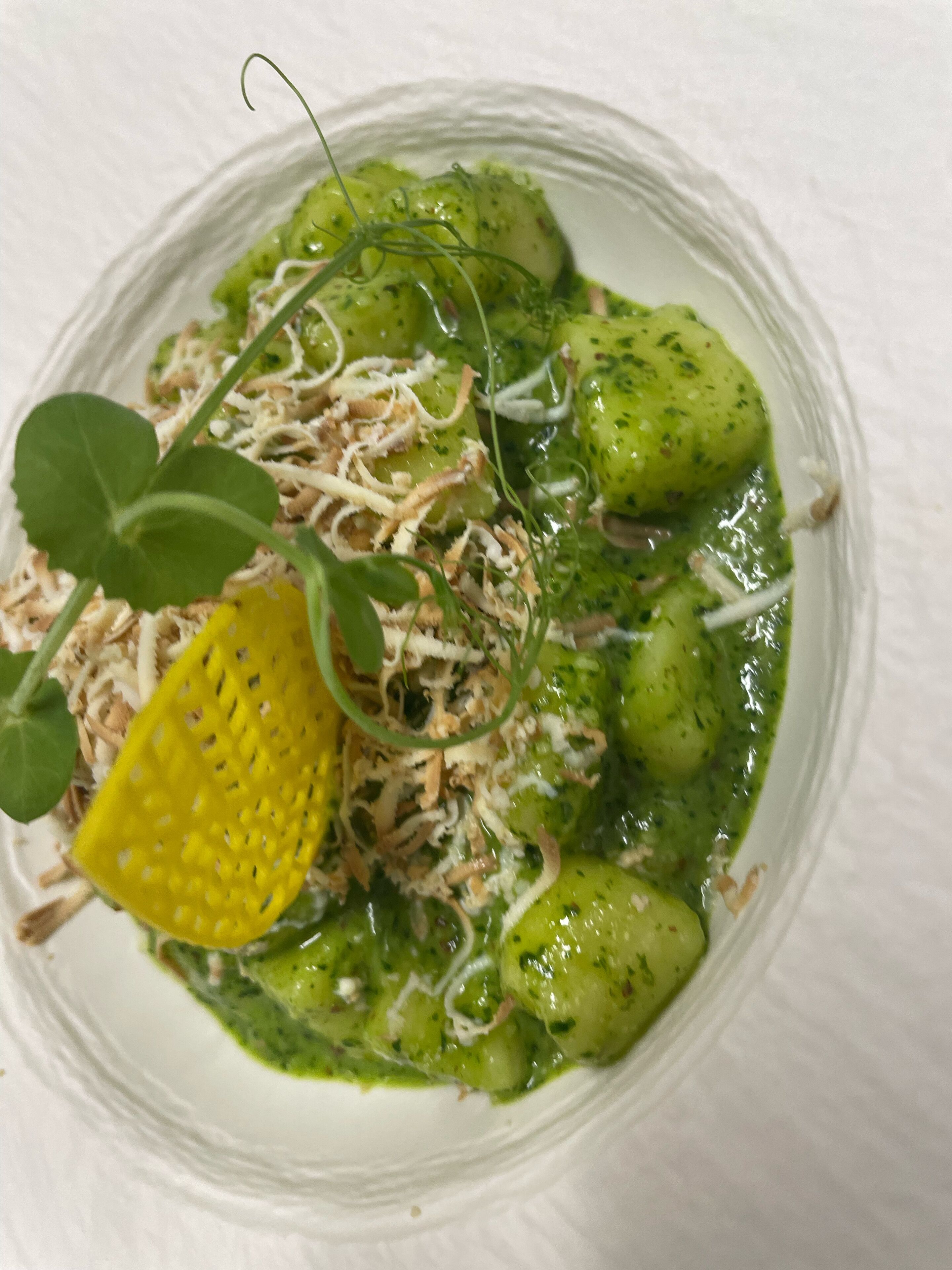 Plat amb salsa verda, verdures i formatge rallat sobre un plat blanc.
