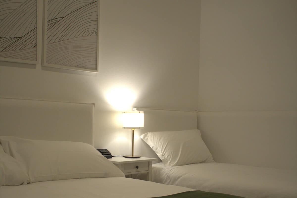 A hotel room with two beds, a nightstand with a lamp, and artwork on the wall.