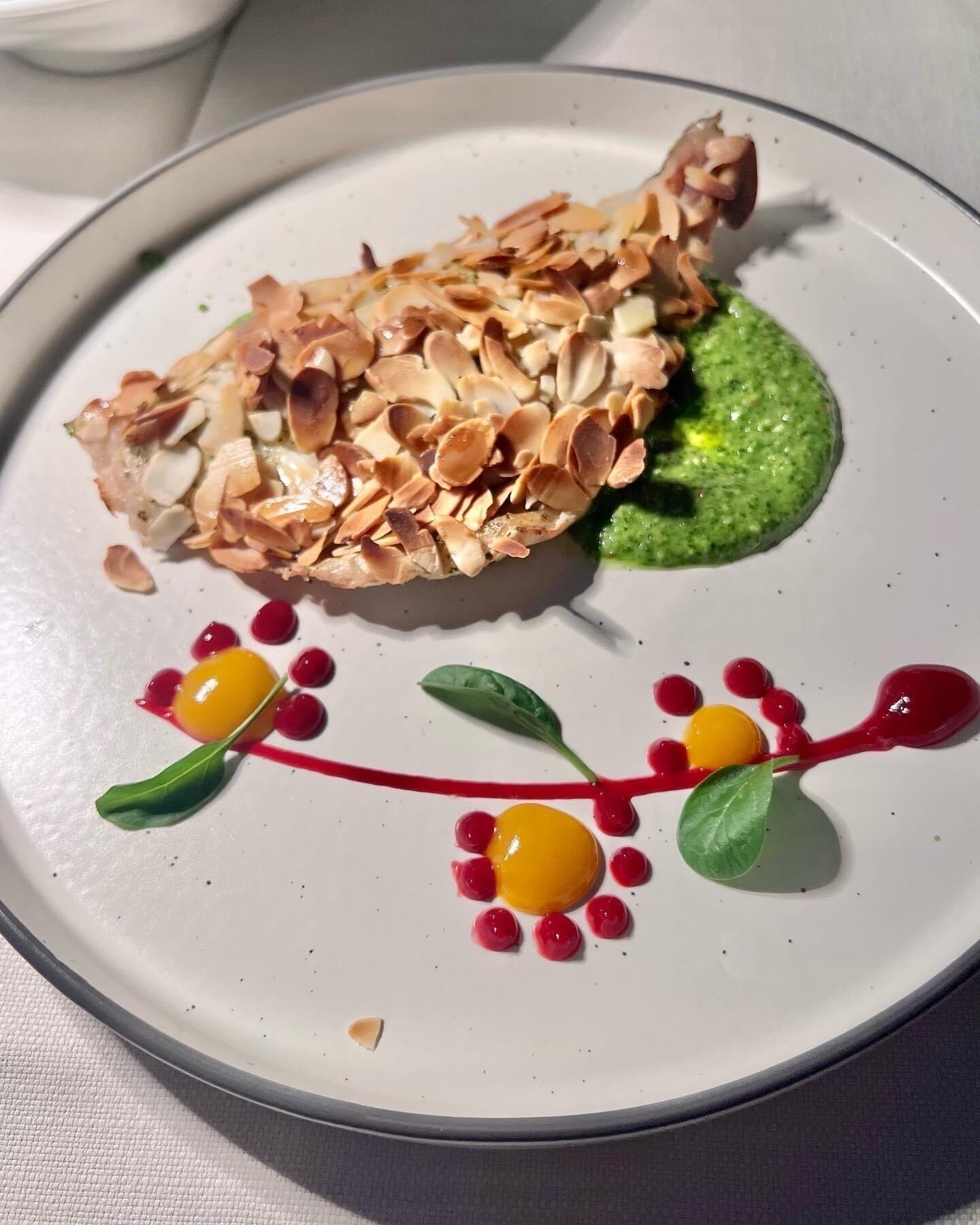 A plate with a dish featuring almonds, green sauce, and decorative elements.
