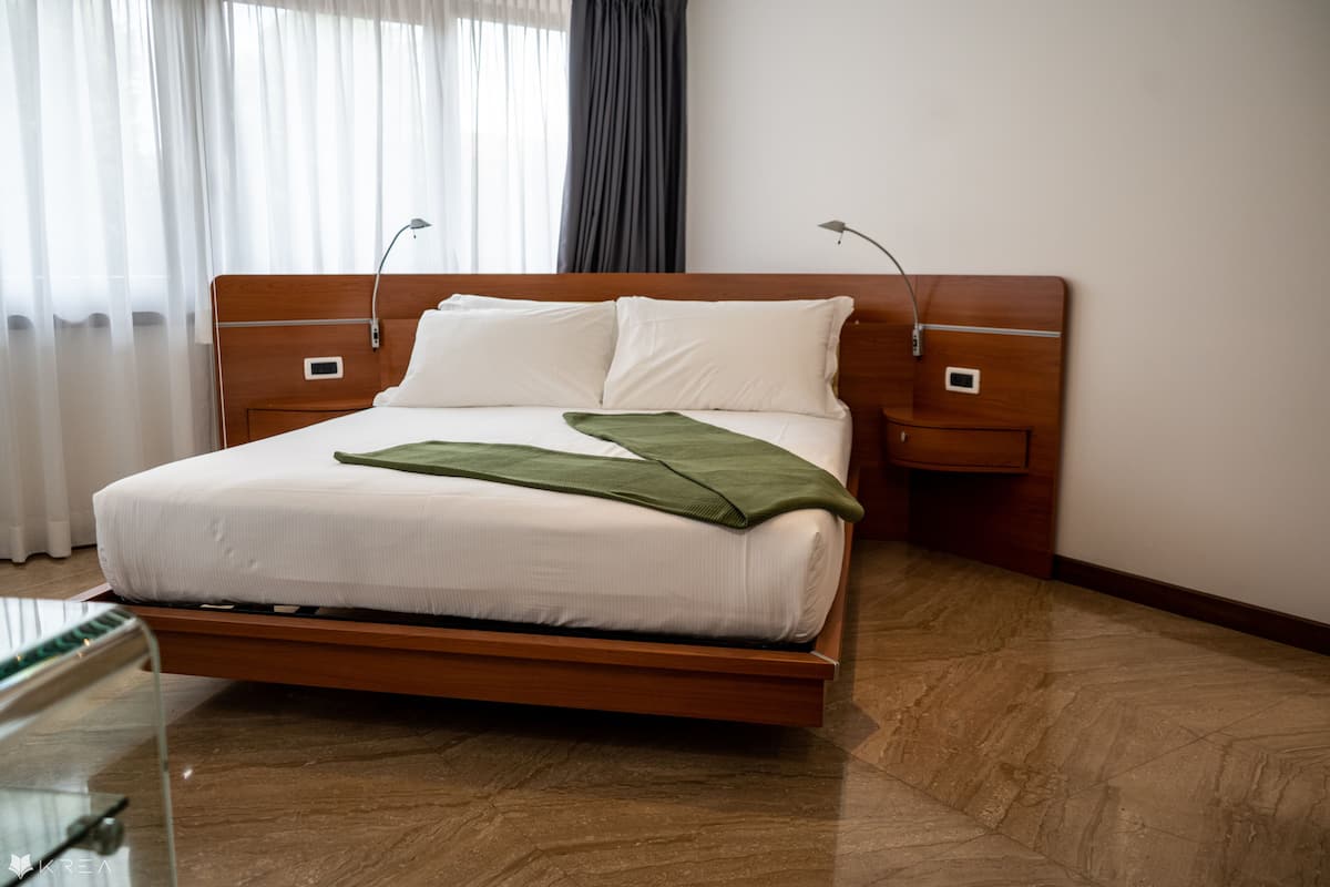 A modern hotel room with a wooden bed, white linens, and a green throw blanket.