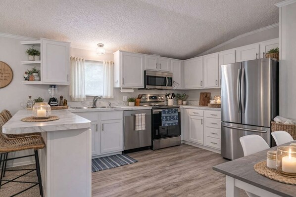 A modern kitchen with white cabinetry, stainless steel appliances, and a central island with seating.