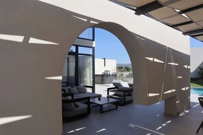An outdoor seating area with sofas and tables, a pool, and a view of a mountain range.