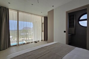 Une chambre d’hôtel avec une grande fenêtre, un lit, un miroir rond et une porte dotée d’une étagère.