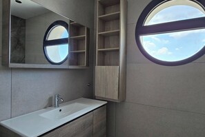 Une salle de bain moderne avec un grand miroir, un lavabo, des meubles en bois et une lucarne.