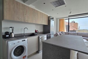 A modern kitchen with a built-in washer, a coffee maker, and a large window with a view of buildings.