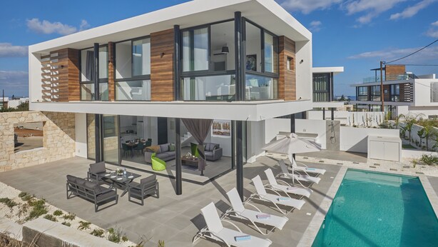 A modern two-story house with a rooftop patio, a swimming pool, and a view of the ocean.