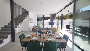 A modern dining area with a wooden table set for four, surrounded by green chairs. A staircase with a black railing is visible to the left.