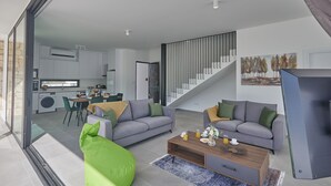 A modern living room with two sofas, a coffee table, and a green bean bag. A staircase leads to an upper level.