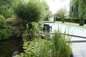 A swimming pool surrounded by lush greenery and a small pond.