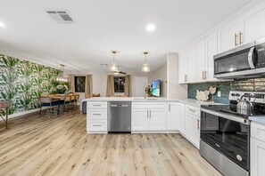 Une cuisine moderne avec des armoires blanches, des appareils en acier inoxydable et un plancher en bois.