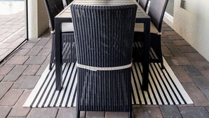 Une terrasse couverte avec une longue table à manger, des chaises en osier noir et des ventilateurs de plafond.