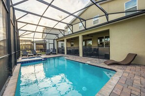 Una piscina con cerramiento de vidrio, sillas de descanso y un área de patio.