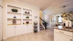Une cuisine moderne avec des meubles blancs, une étagère intégrée et un luminaire suspendu.