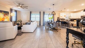 Un salon moderne avec un ensemble de canapés, un coin repas avec une longue table et une cuisine en arrière-plan.