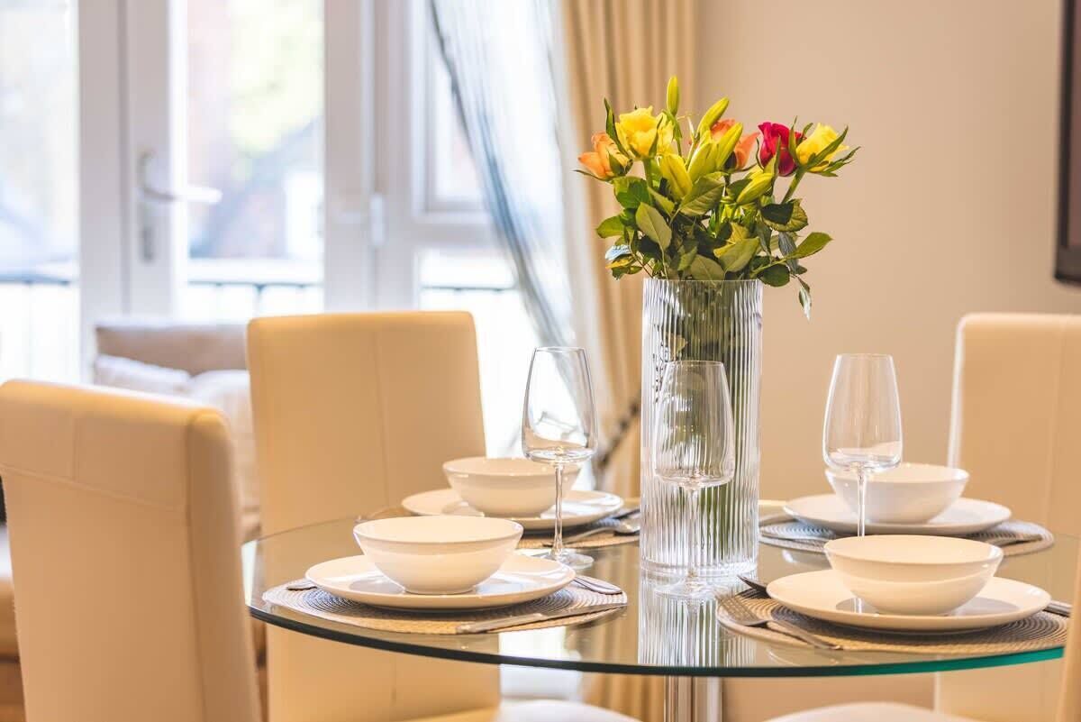 A dining table with white plates, clear glassware, and a vase with flowers.