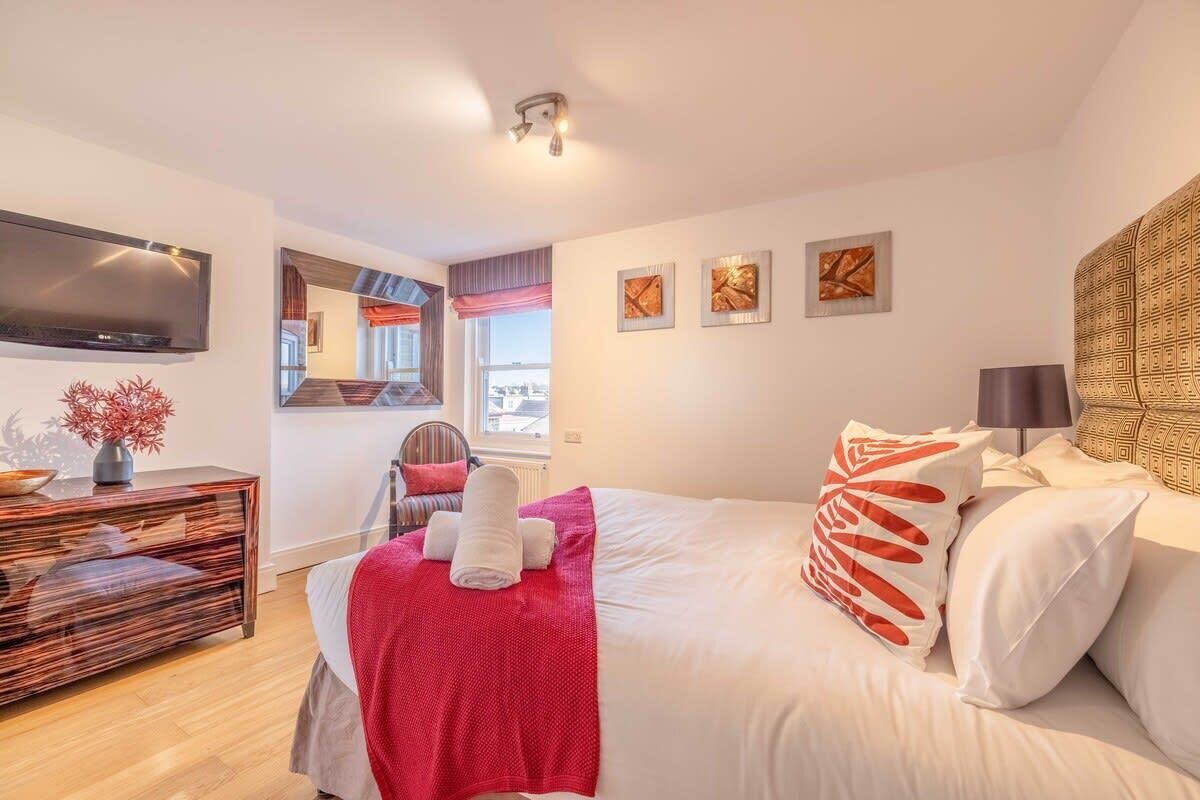 A modern hotel room with a bed, a flat-screen TV, a desk with a lamp, and artwork on the walls.