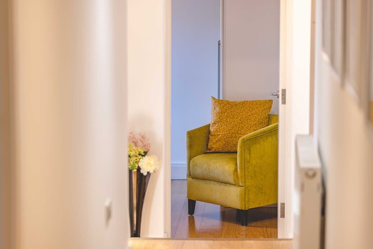 Een kamer met een groene fauteuil, een vaas met bloemen en een witte deur.