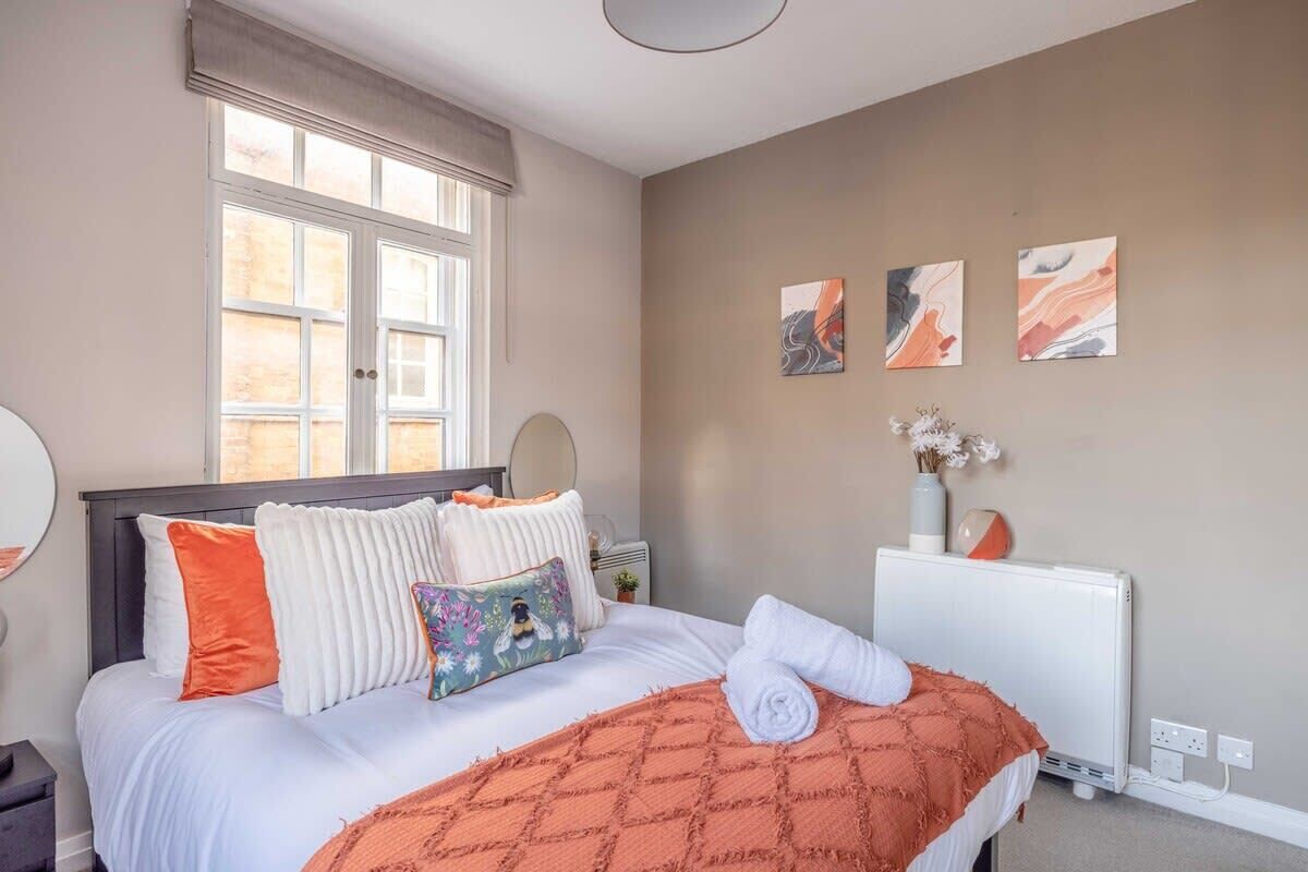 A bedroom with a bed, a window, a radiator, and three wall-mounted artworks.