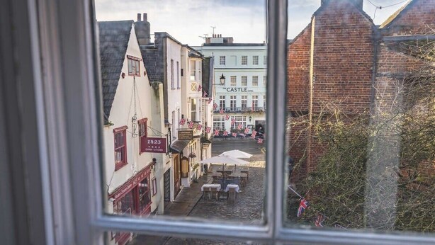 Una calle empedrada con edificios, un letrero que dice 'The Castle Hotel' y mesas al aire libre.