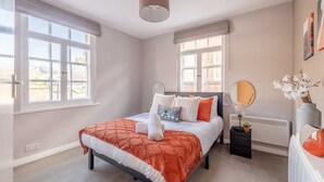 Un dormitorio con una cama, una mesita de noche, un espejo y una ventana.