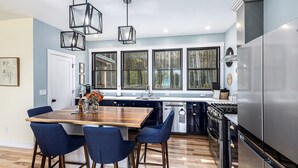 Een moderne keuken met een houten eiland, blauwe barkrukken, roestvrijstalen apparatuur en grote ramen.