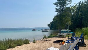 Een strand met witte ligstoelen, een picknicktafel en boten op het water.