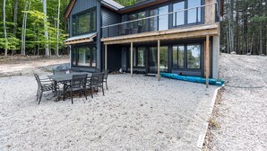 Een modern huis met twee verdiepingen en een terras, omgeven door bos.