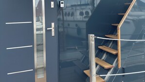 A modern interior with a dark blue door, a glass door leading to a deck, and a wooden staircase. - Premium Hausboot Blaue Lagune (Lübeck)