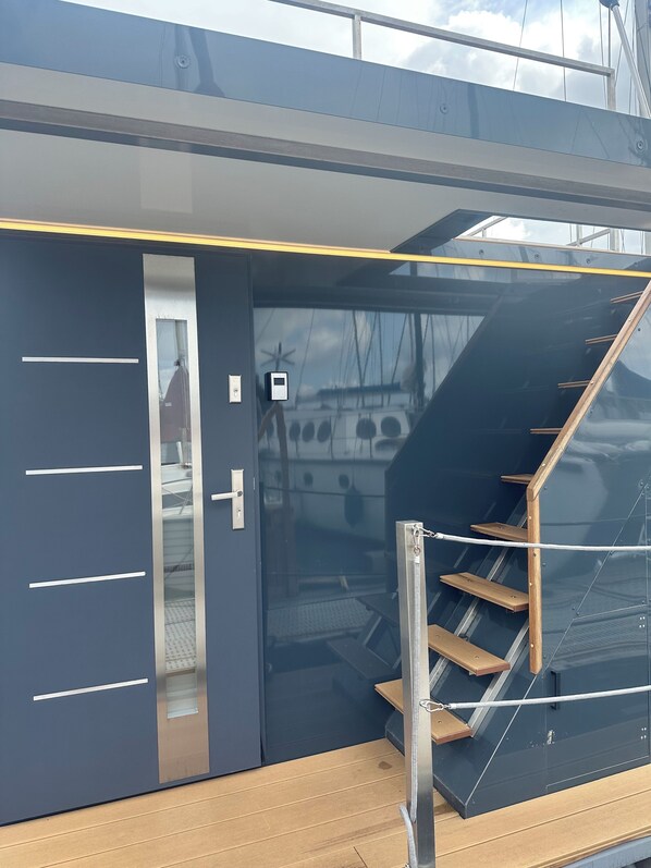 A modern interior with a dark blue door, a glass door leading to a deck, and a wooden staircase.