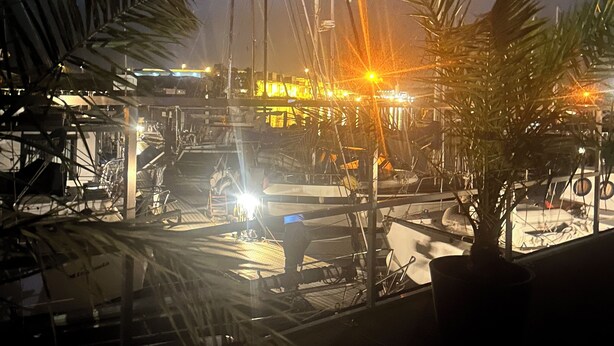 A marina at night with boats docked, palm trees, and a brightly lit building in the background. - Premium Hausboot Blaue Lagune (Lübeck)