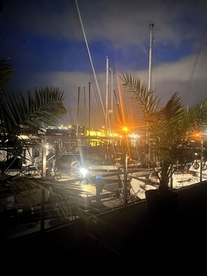 A marina at night with boats docked, palm trees, and a brightly lit building in the background.