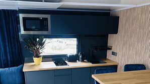 A compact kitchen with a microwave, toaster, and kettle on a wooden countertop. There is a blue sofa with a cushion and a small rug on the floor. - Premium Hausboot Blaue Lagune (Lübeck)