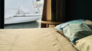 A room with a bed, a view of a sailboat, and a window with curtains. - Premium Hausboot Blaue Lagune (Lübeck)