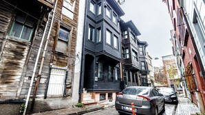 A narrow street with multi-story buildings, a parked car, and a visible fire hydrant.