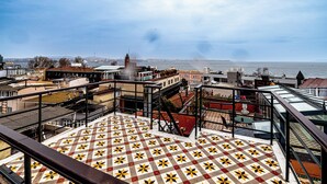 A rooftop terrace with a patterned floor, overlooking a cityscape and a body of water.