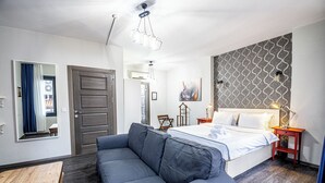 A modern bedroom with a large bed, a grey sofa, a wooden table, and a patterned wall.
