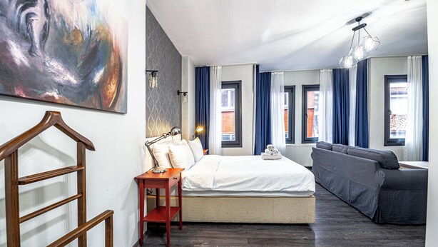 A modern hotel room with a large bed, a sofa, a wooden chair, a desk, and a painting on the wall.