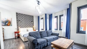 A modern living room with a grey sofa, a wooden coffee table, and a bed with a white headboard.